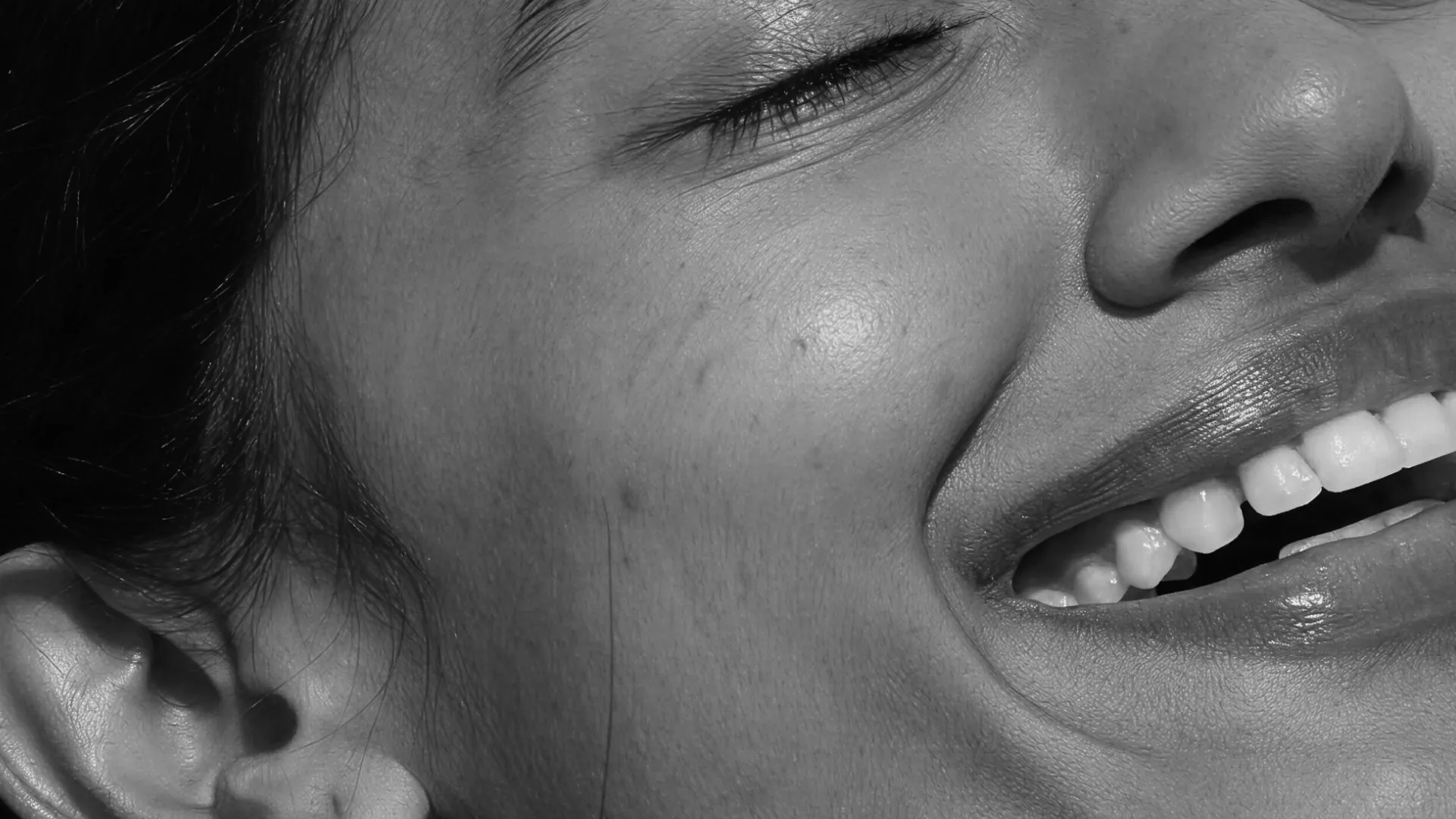 Close-up black-and-white photograph of a smiling woman's cheek, mouth and skin in raking light